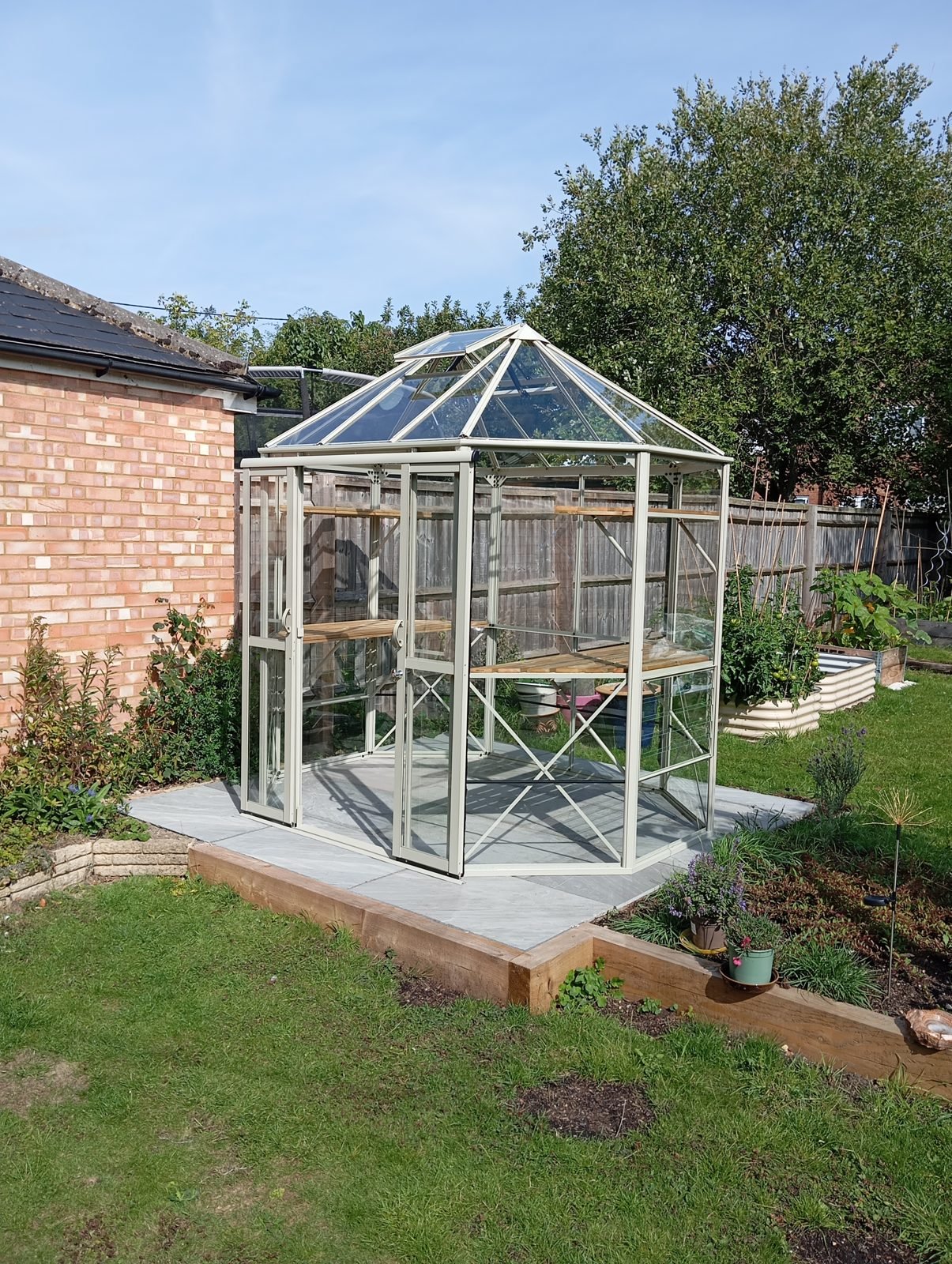 Finished greenhouse in a garden beside a brick garage