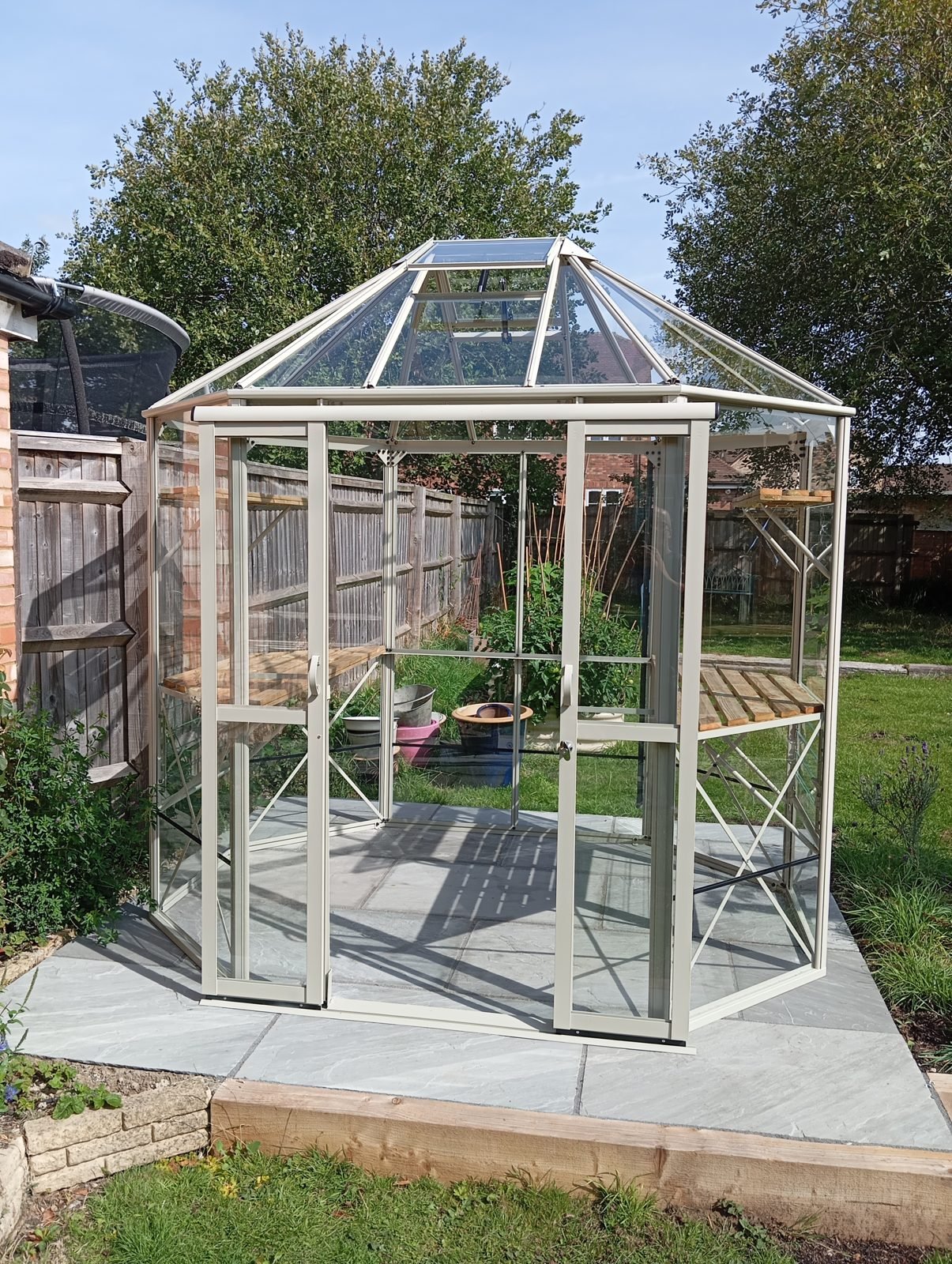 Finished aluminium greenhouse with glass roof and sliding doors on a paved base
