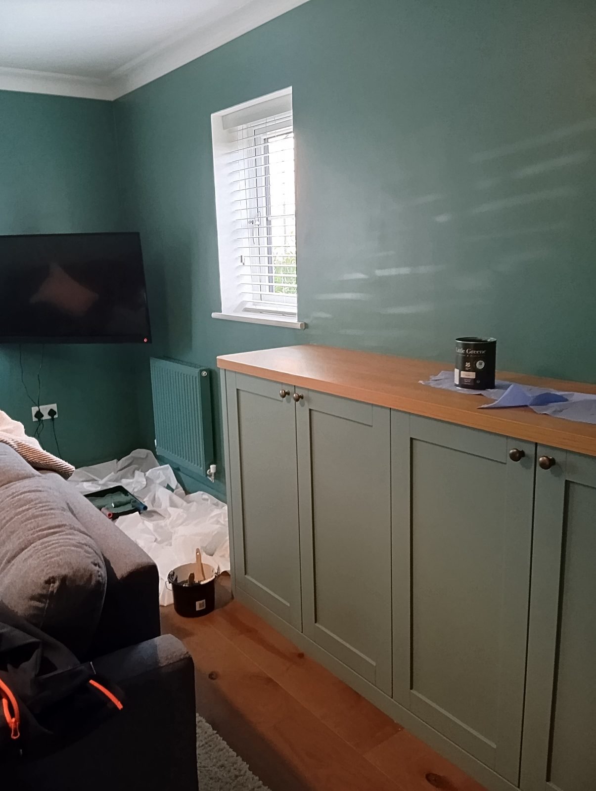 Sage green cupboards beneath a window in a deep green living room