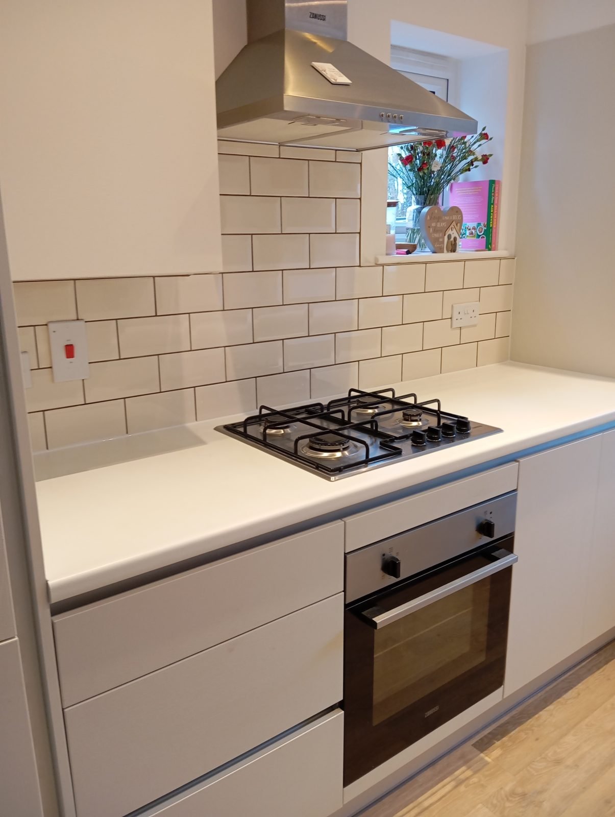 Finished white metro tile splashback behind a gas hob with contrasting grout